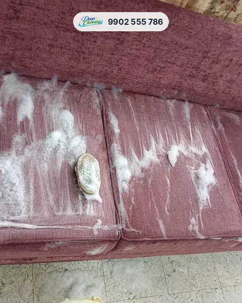 Three-seater fabric sofa covered in shampoo foam with a brush