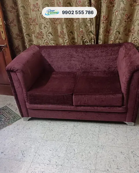 Maroon fabric two-seater sofa in front of floral curtains